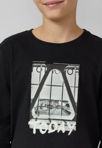 Czarna bluza z dużym nadrukiem przedstawiającym monochromatyczną scenę lotniska oraz białym napisem „TODAY” w nadruku o fakturowanej powierzchni. Gładka tkanina.