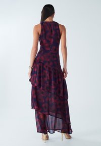 Dlouhé šaty bez rukávů z průhledné látky s vrstveným asymetrickým lemem. Tmavě fialové s červenými květinovými vzory. Zapínání na zip vzadu.