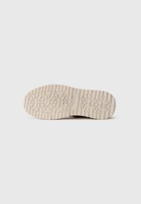 Semelle d'une chaussure beige avec des motifs de semelle triangulaires et rectangulaires profonds, taille 32, marquée "superfit" au centre.
