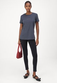 Sötétkék pamut póló rövid ujjal, hímzett logóval, fekete skinny farmernadrággal és piros válltáskával párosítva. Fekete lapos cipőkkel egészül ki a megjelenés.