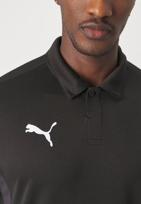 Čierna polo košeľa vyrobená z textúrovaného materiálu, s dvojitým zapínaním a bielym logom Puma na ľavej hrudi.