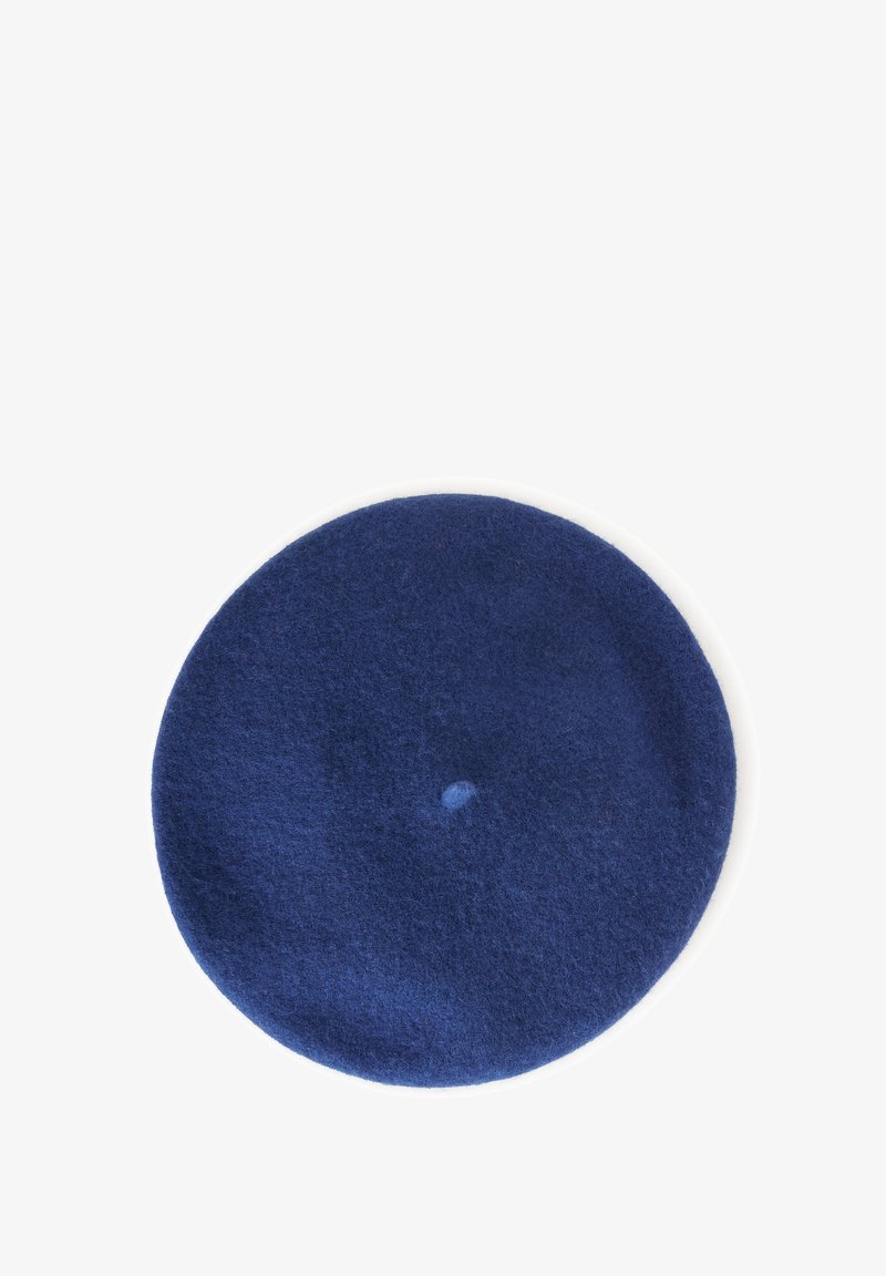 Kulatý námořnický modrý vlněný baret s malým středovým výstupkem, zobrazený na bílé větě.