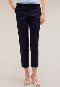 Marineblauwe broek met een getailleerde pasvorm, cropped lengte, gladde stof en voornaad detail. Gecombineerd met witte sleehakken.