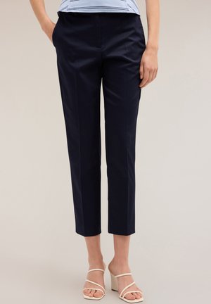 Marineblauwe broek met een getailleerde pasvorm, cropped lengte, gladde stof en voornaad detail. Gecombineerd met witte sleehakken.