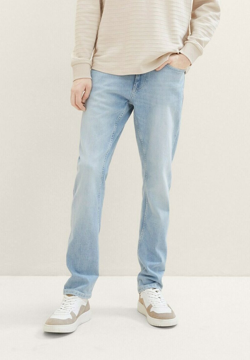 Hellblaue Jeans mit gerade geschnittenem Bein, vorderen Taschen und dezenten Ausbleichungen, kombiniert mit weißen und beigen Sneakers.