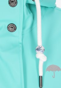 Török rózsaszín esőkabát fehér húzózsinórral és egy kék mintás díszgombbal. Ezüst ernyő logó elöl.