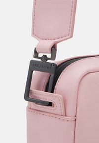 Correa de bolsa sintética rosa con una textura lisa, que presenta una hebilla metálica negra y detalles de costuras visibles.