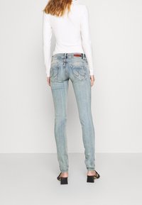 Světle modré džíny s úzkým střihem, obsahující zadní kapsy a jemnou vybledlou texturu. Kombinované s slim fit bílým tričkem s dlouhým rukávem.