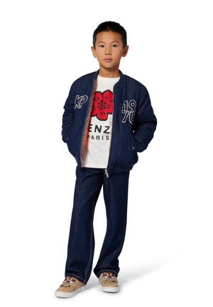 Blaue Denim-Bomberjacke mit bestickten Akzenten, weißes T-Shirt mit einem roten Blumenmuster, dunkle Denim-Jeans und beige Sneaker mit einem Tigerdesign.