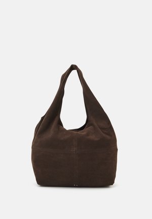 Brązowa zamszowa torba na ramię z szerokim paskiem i miękką, luźną konstrukcją, stojąca pionowo na jednolitym jasnym tle.