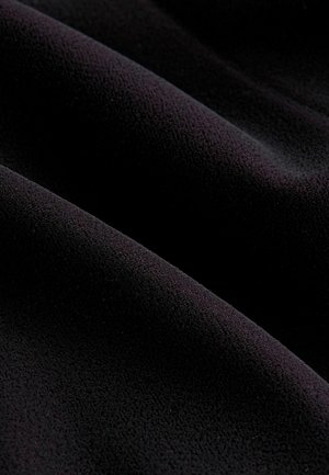 Černá tkanina s hladkým, texturovaným povrchem, s jemnými vlnami a záhyby. Materiál vypadá měkce a plyšově.