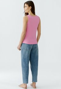 Pink ribbed tank top with a round neckline, paired with light blue baggy jeans. Flat sandals and large earrings complete the outfit.