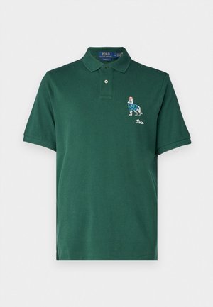Polo de color verde oscuro hecho de algodón. Cuenta con un collar, botones grabados y un gráfico bordado de un perro con un suéter a rayas.