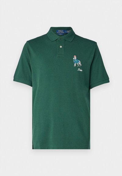 Dark green polo shirt made of cotton. Features a collar, embossed buttons, and an embroidered graphic of a dog in a striped sweater.