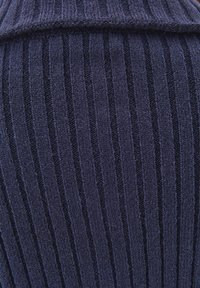 Navy neulottu kangas, jossa on pystysuora ribbitekstuuri. Materiaali on pehmeä ja näkyvillä on ompeleita, mikä luo yksityiskohtaisen ja tekstuurisen ilmeen.