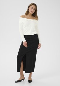 Off-White schulterfreies Oberteil mit Knoten-Detail, kombiniert mit einem schwarzen Jeansrock mit einem Schlitz vorne und schwarzen Absatzmules.