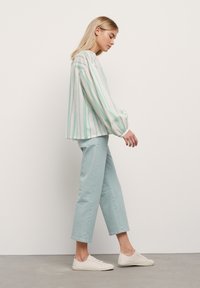 Chemisier rayé en blanc, vert et bleu associé à un pantalon court bleu clair et des baskets blanches. Le chemisier possède des manches ballon et une coupe loose.