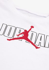 Vit bomull t-shirt med en stor röd "Jumpman" logotyp och "JORDAN" text i fet svart stil. Slät tyg med en rundad halsdesign.