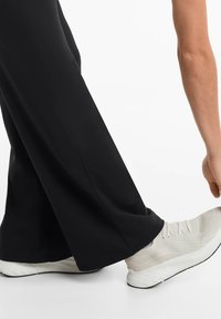 Schwarze weite Hosen mit glatter Textur, kombiniert mit hellgrauen Sportschuhen mit strukturiertem Obermaterial und weißer Sohle.