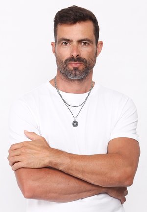 Collana con ciondolo a forma di bussola in argento; il modello indossa una t-shirt bianca e ha capelli scuri ordinatamente pettinati e una barba.