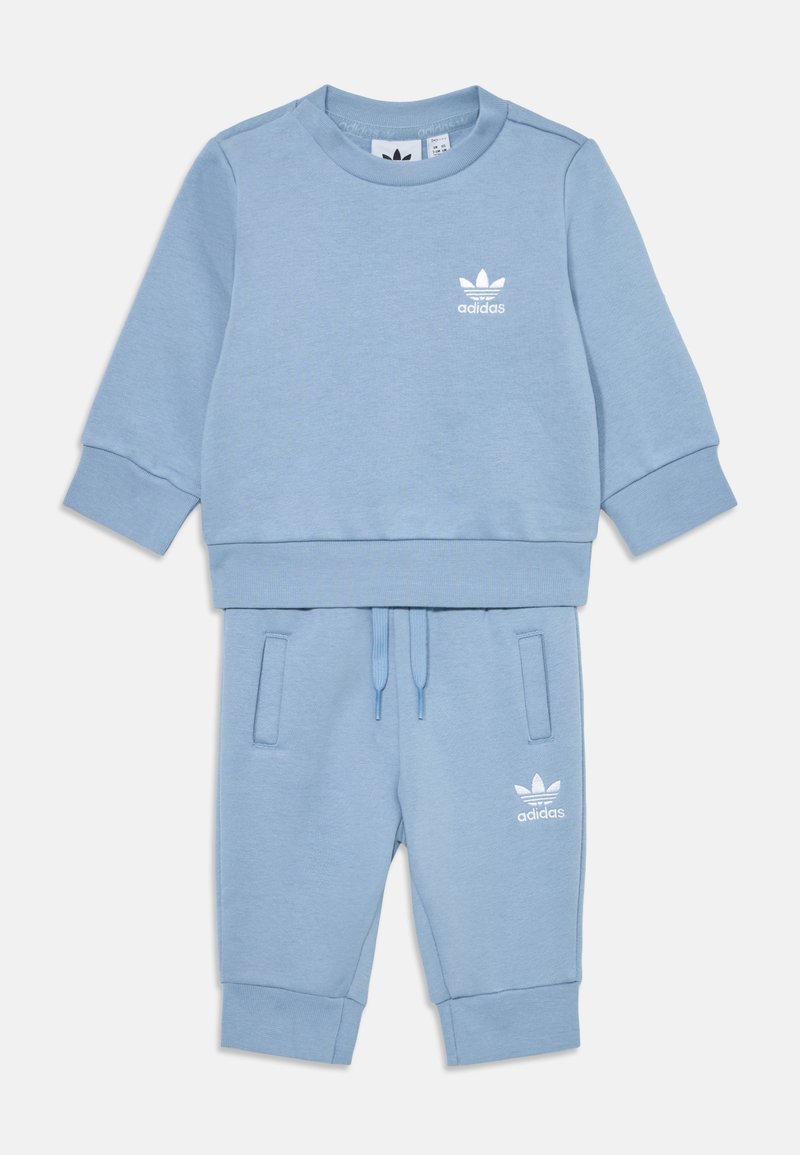 Conjunto de sweatshirt e calças de fato em azul claro, feito de tecido macio, com punhos e cós em ribana. Apresenta o logótipo branco da Adidas em ambas as peças.