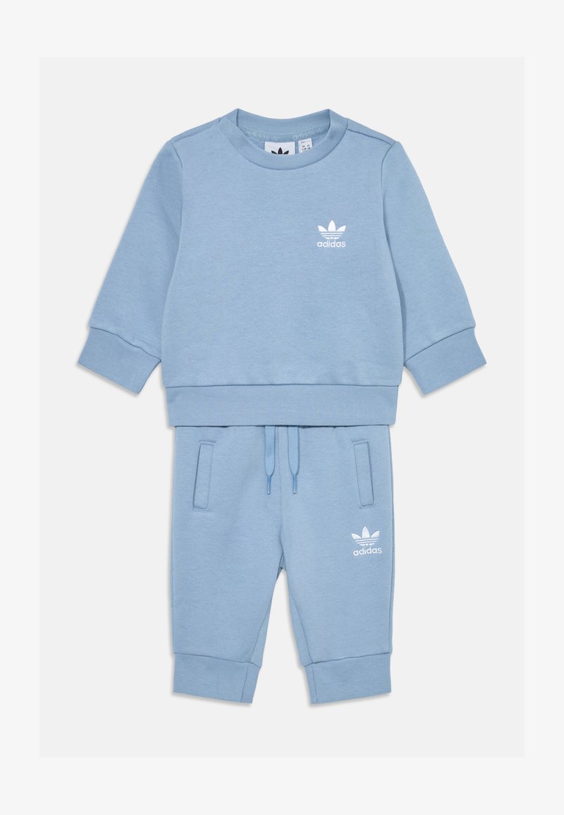 Svetlomodrý športový set so svetrom a teplákmi vyrobený z jemného materiálu, s rebrovanými manžetami a pásom. Obsahuje biele logo Adidas na oboch kusoch.