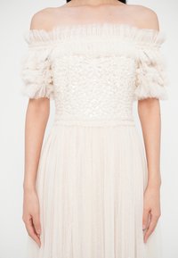 Robe blanche épaule dénudée avec sequins floraux sur le corsage, manches courtes en voile à volants, et jupe en tulle plissée.