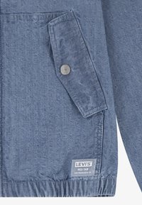 Ljusblå denimjacka med en strukturerad yta, med en ficka med knappslut och en logopatch märkt "LEVI'S RED TAB."