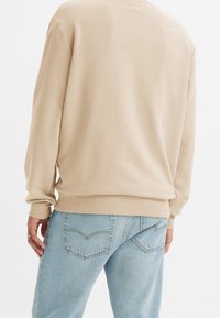 Beige sweatshirt med långa ärmar, avslappnad passform, mjuk textur och ribbade ärmslut, ihop med ljusblå denimjeans med bakfickor.