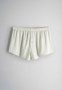 Boxeri pentru bărbați din bumbac alb, cu talie elastică și trei nasturi în față, așezați întinși pe un fundal gri deschis.