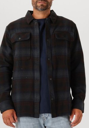 Zwart en grijs geruite flanellen shirt met twee borstzakken, knopen sluiting aan de voorkant en kraag. Gedragen over een marineblauw T-shirt. Casual pasvorm.