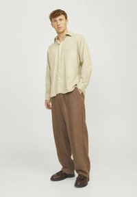 Helle beige Langarm-Hemd mit Knöpfen, kombiniert mit lockeren braunen Hosen und dunklen Schuhen; glattes Material mit lässiger Passform und klassischem Design.