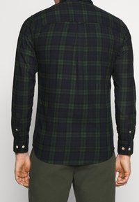 Rutig skjorta i mörkgrön och marinblå, långa ärmar, knäppning i ärmsluten, tillverkad av fleece med böjd nederkant och en skärning bak för rörlighet.