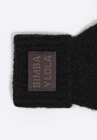 Czarny wełniany szalik z teksturowanym, dzianym wzorem. Posiada prostokątną skórzaną naszywkę z wytłoczonym napisem: "BIMBA Y LOLA."