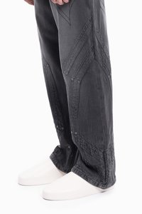 Ciemnoszare dżinsy o luźnym kroju, z teksturowanymi, skośnymi szwami i guzikami napami, w połączeniu z białymi, gładkimi, minimalistycznymi butami.