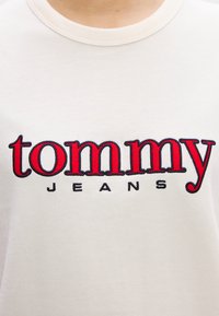 Biała bawełniana koszulka z wyhaftowanym czerwonym napisem "tommy" oraz czarnym napisem "JEANS" poniżej, z klasycznym okrągłym dekoltem.
