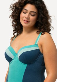Maillot de bain dans des teintes de bleu sarcelle et marine, présentant un tissu texturé, des bonnets avec armatures et des bretelles réglables, avec une finition lisse et un design en blocs de couleur.