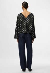 Blusa negra con lunares, con un escote en V profundo, mangas largas y un corte holgado, combinada con jeans de pierna ancha de cintura alta en azul oscuro.