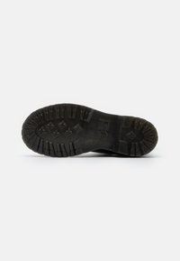 Sole de cizmă din cauciuc neopren negru, cu tălpi adânci, având o suprafață groasă, texturată și caneluri pronunțate pentru aderență. Design compact și robust.
