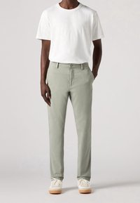 Ljusgrå chinos med rak ben-design, tillverkade av bomullsblandat tyg, kombinerade med en vit t-shirt med kort ärm och beige sneakers.