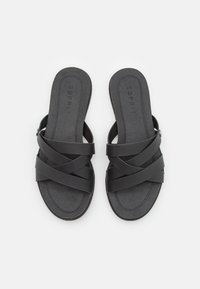 Black slide sandals with crisscross straps, made of smooth material, featuring a textured insole and subtle logo detail on the footbed.