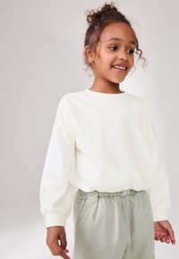 Sweat-shirt blanc manches longues avec coupe ample et poignets côtelés, associé à un pantalon vert clair à cordon de serrage avec fermeture à bouton.