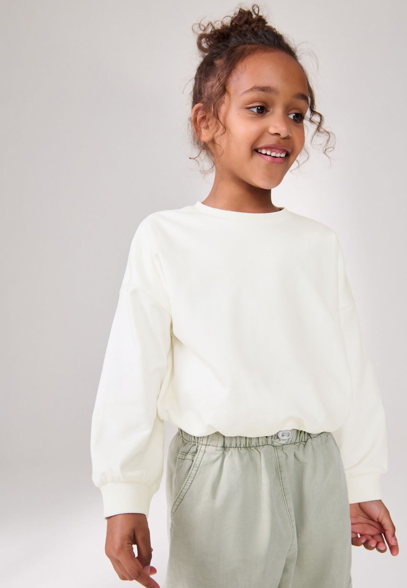 Sweat-shirt blanc manches longues avec coupe ample et poignets côtelés, associé à un pantalon vert clair à cordon de serrage avec fermeture à bouton.