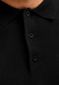 Polo shirt nera con una texture a maglia, dotata di colletto e tre bottoni neri in plastica al collo.