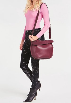 Borsa in pelle bordeaux con una texture morbida, forma arrotondata e pattina superiore. Abbinata a un top rosa a coste e jeans neri con motivo.