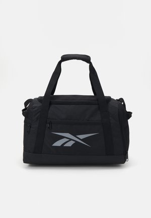 Svart duffelbag med glidelås, med robuste håndtak, justerbar skulderrem og et reflekterende logo på frontpanelet.