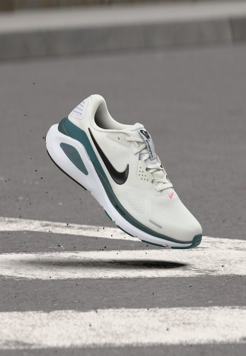 Λευκό και τιρκουάζ παπούτσι για τρέξιμο της Nike στον αέρα πάνω από άσφαλτο με λευκές σηματοδοτήσεις δρόμου και μικρά υπολείμματα γύρω από την σόλα.