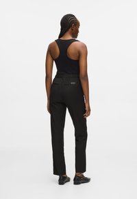 Μαύρο αμάνικο κοντομάνικο, ψηλόμεσα μαύρα παν trousers με ελαστική μέση, δύο πίσω τσέπες με φερμουάρ και μαύρα διακοσμητικά παπούτσια.