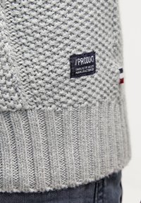 Gray knitted sweater with a textured pattern, featuring a stitched label with "#PRODUKT" and "INDUSTRIALLY MANUFACTURED" details.