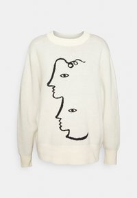 Krämsvett som har en svart grafisk design av abstrakta ansikten och  ögon. Rundad hals, långa ärmar och ribbad nederkant och ärmslut.